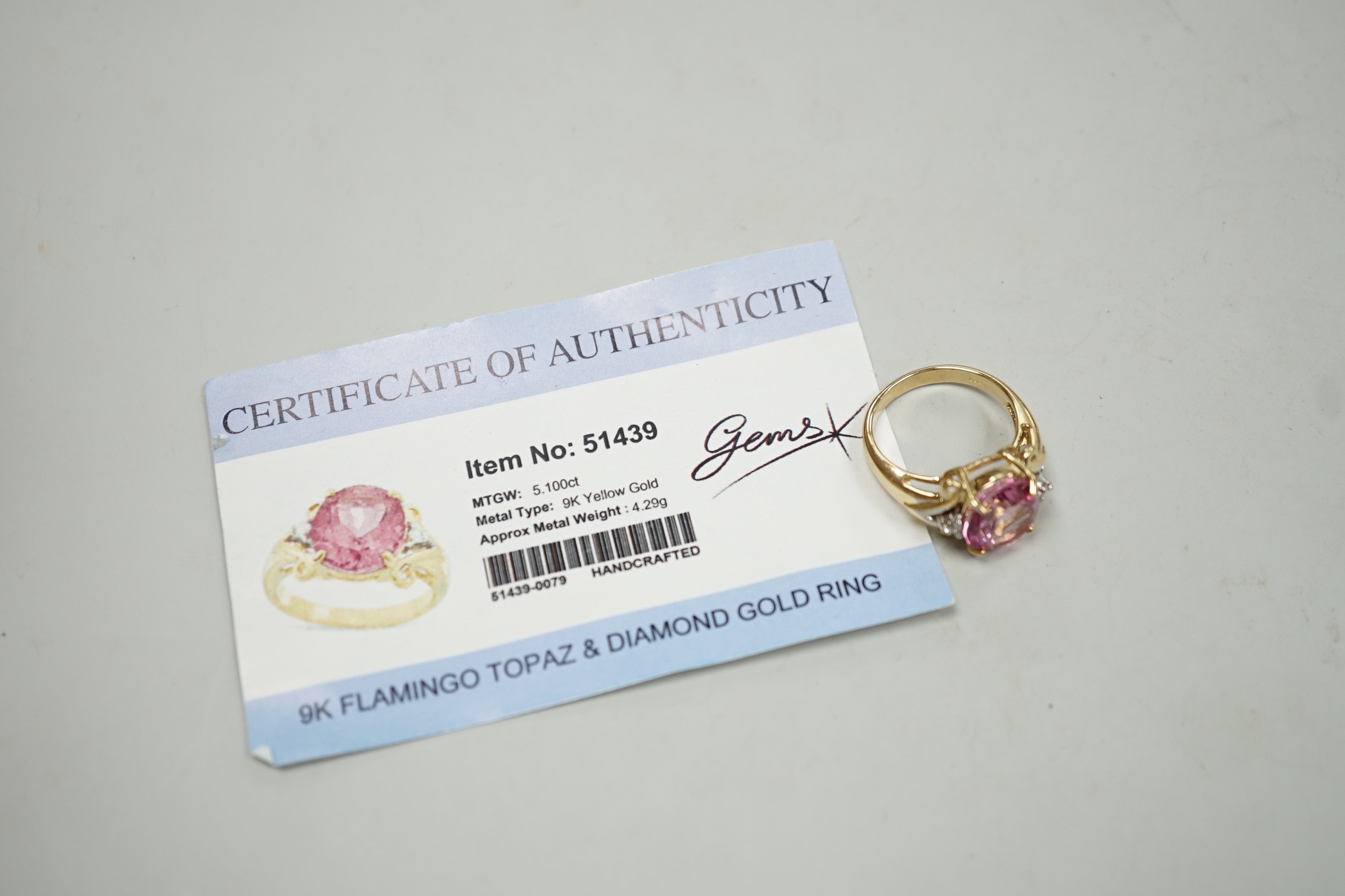 A modern 9ct gold and single stone oval cut flamingo topaz dress ring with two stone diamond set shoulders, size N, gross weight 5.3 grams, with Gems TV certificate.